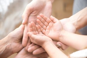 Zbliżenie na dłonie dorosłych i dzieci, ułożone razem w geście troski i wsparcia.