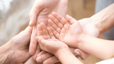 Zbliżenie na dłonie dorosłych i dzieci, ułożone razem w geście troski i wsparcia.